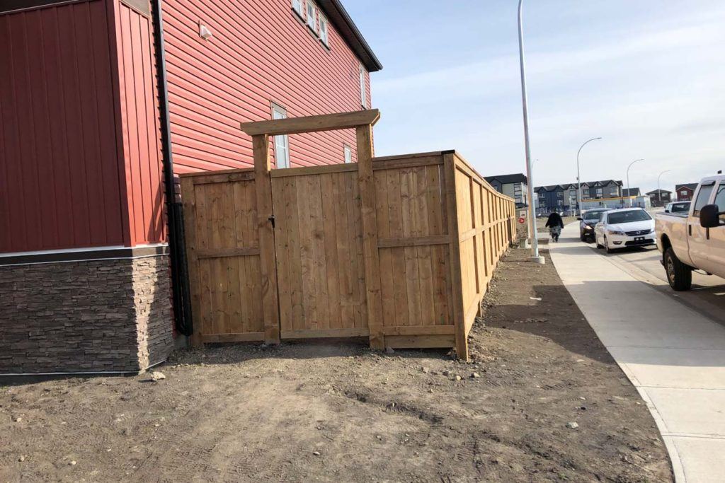 a wooden gate at the side of a house with red siding