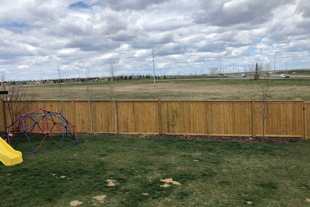 a wooden fence in a backyard in front of an empty field