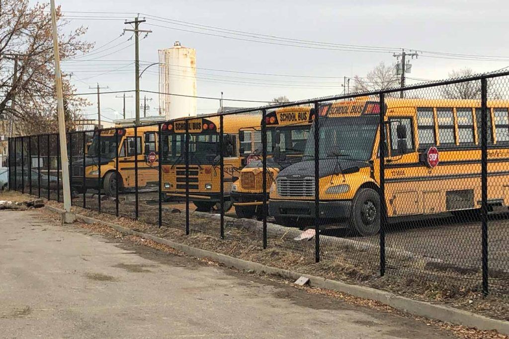 a black chain link fence with four yellow school buses behind it